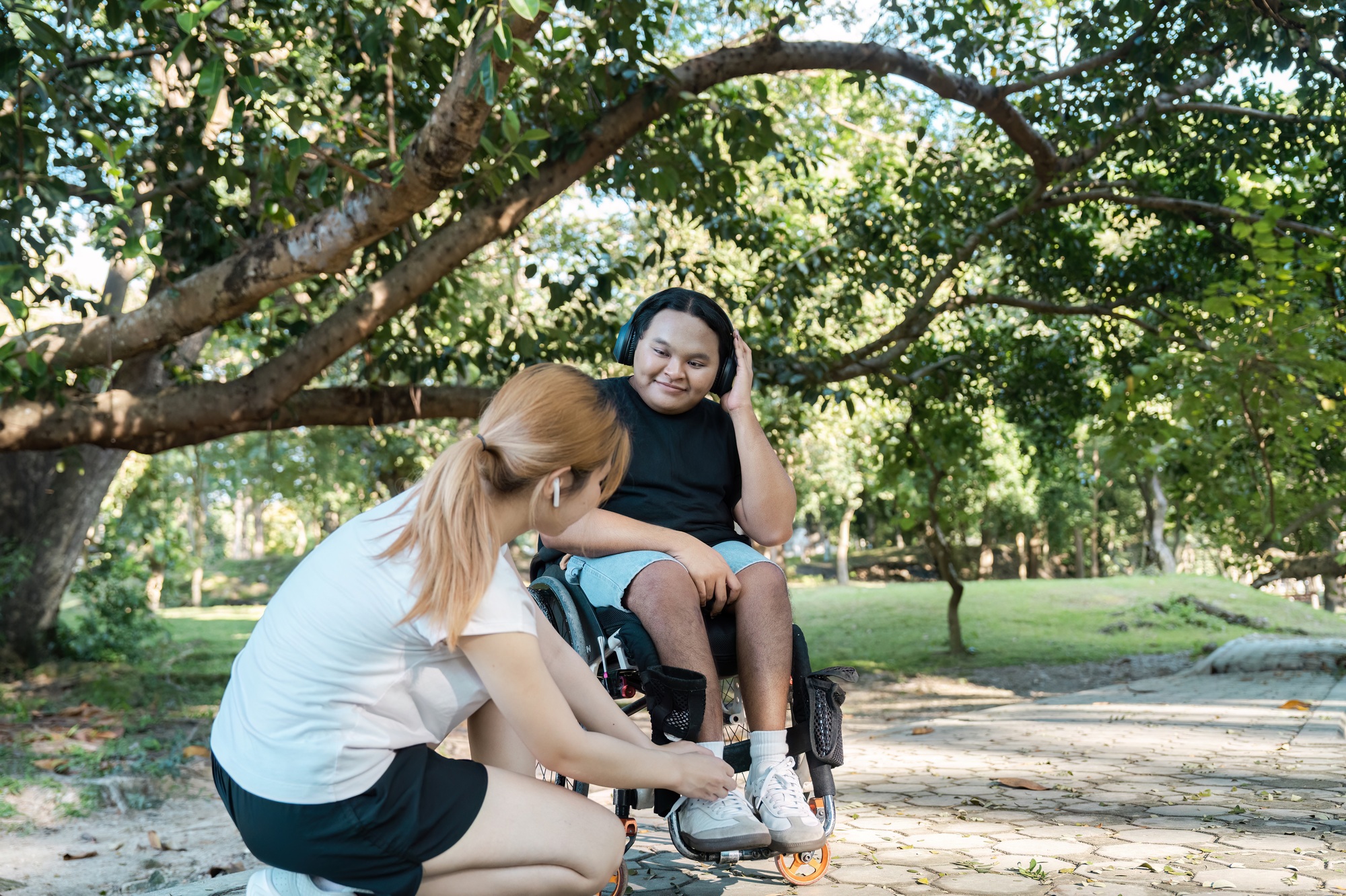 Inclusive Outdoor Activity: Young Woman Assisting a Smiling Man in a Wheelchair Enjoying a Sunny Day